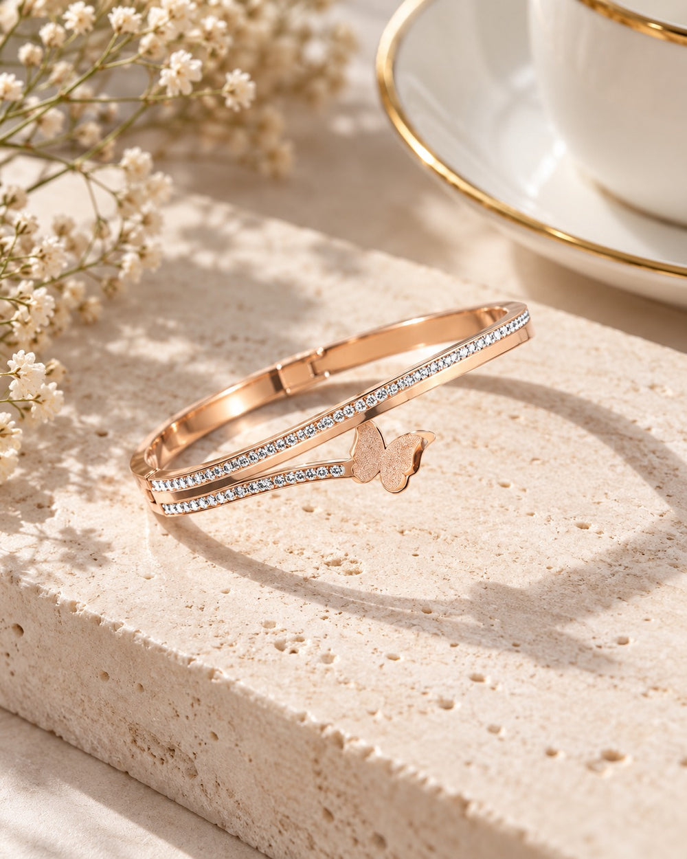 Butterfly Bracelet Classic Cuff Rose Gold trên mặt đá cạnh tách trà và hoa baby