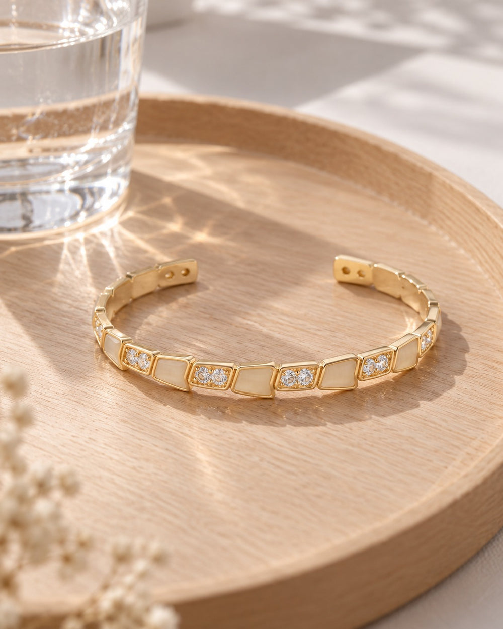 Lyz & Liam Viper Cuff Gold trên khay gỗ cạnh ly nước