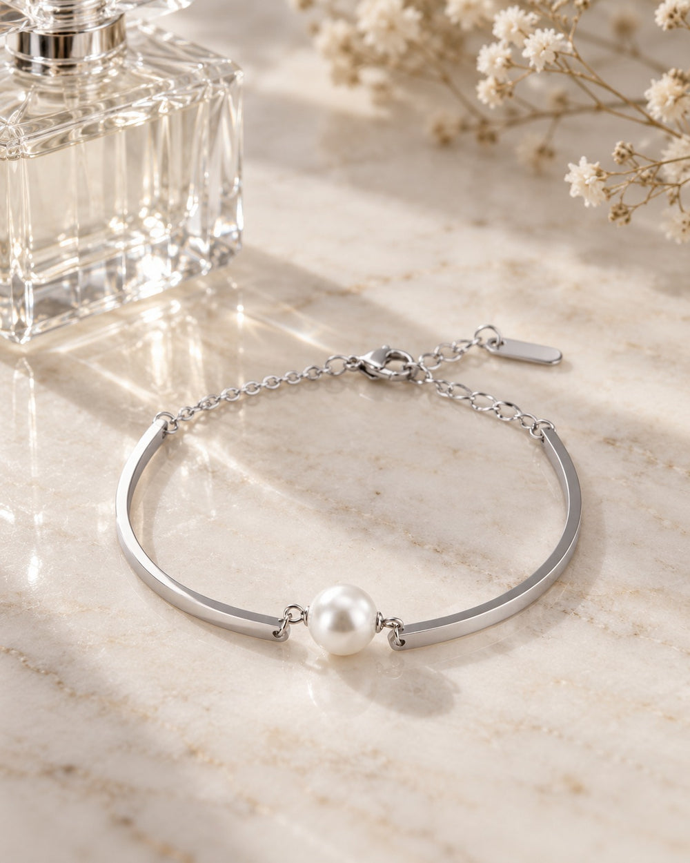 Pearl Bracelet Silver trên mặt đá cạnh lọ nước hoa và hoa baby