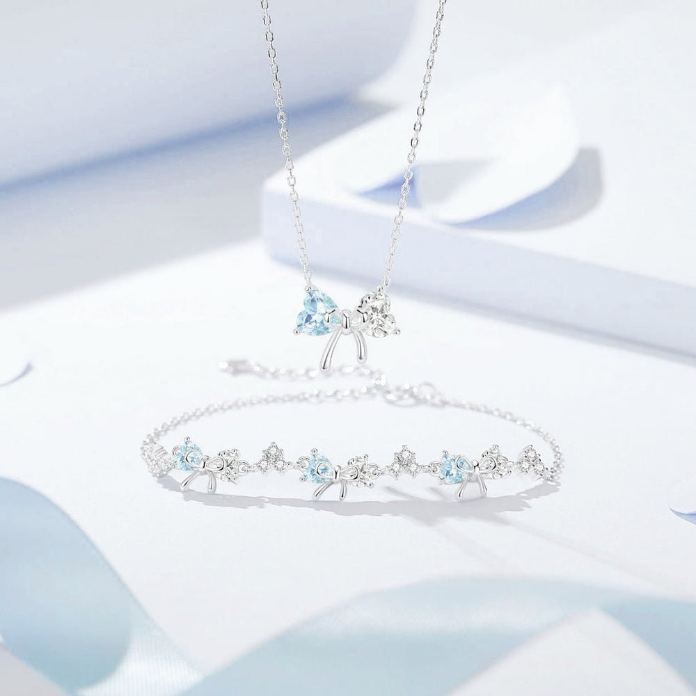 Crystal Bow Necklace & Bracelet Set Silver, gồm dây chuyền mặt nơ đá xanh nhạt và lắc tay xếp hàng hoa đá nhỏ xanh trắng xen kẽ